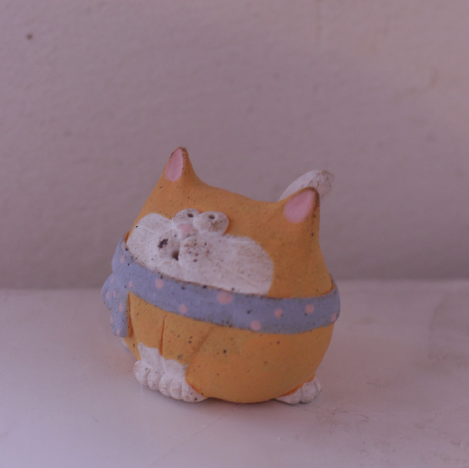 Handmade clay cat figurine with orange and white colors wearing a blue polka dot scarf