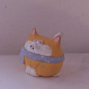 Handmade clay cat figurine with orange and white colors wearing a blue polka dot scarf