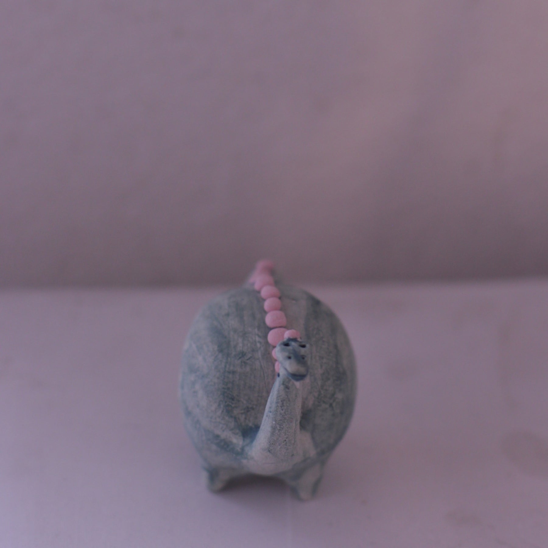 Handmade pottery animal figurine of a dinosaur with a gray body and pink dots along its back