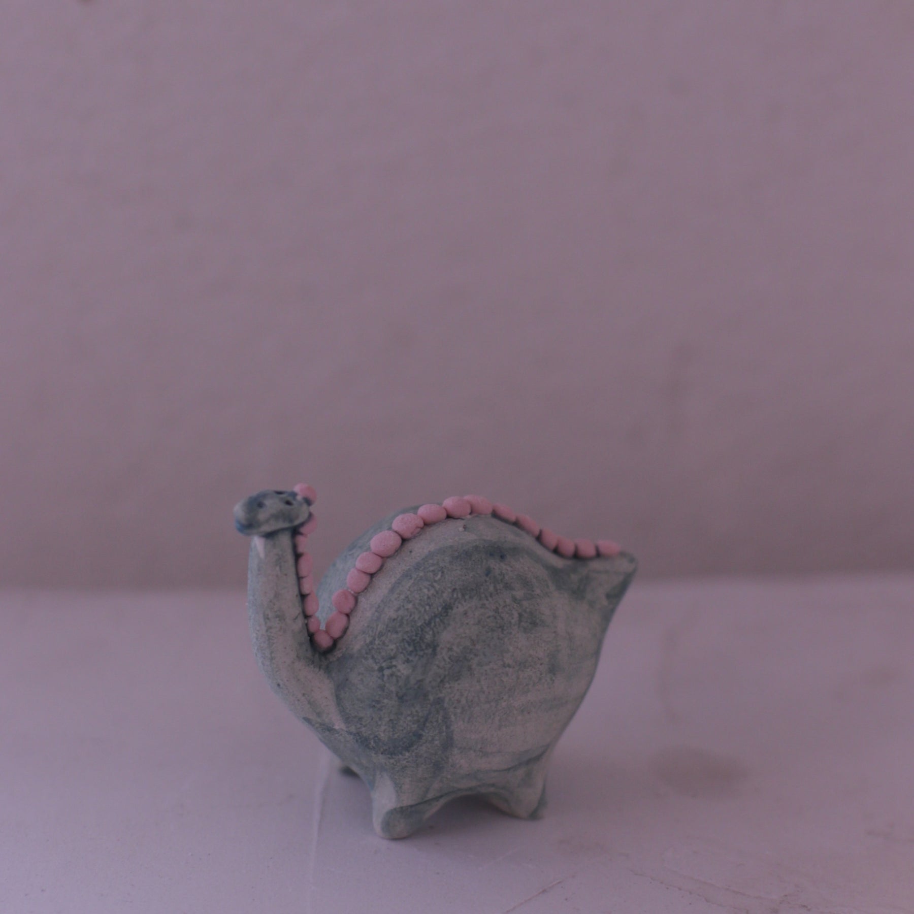 Handmade pottery animal figurine shaped like a gray dinosaur with pink accents