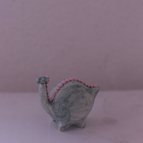 Handmade pottery animal figurine shaped like a gray dinosaur with pink accents