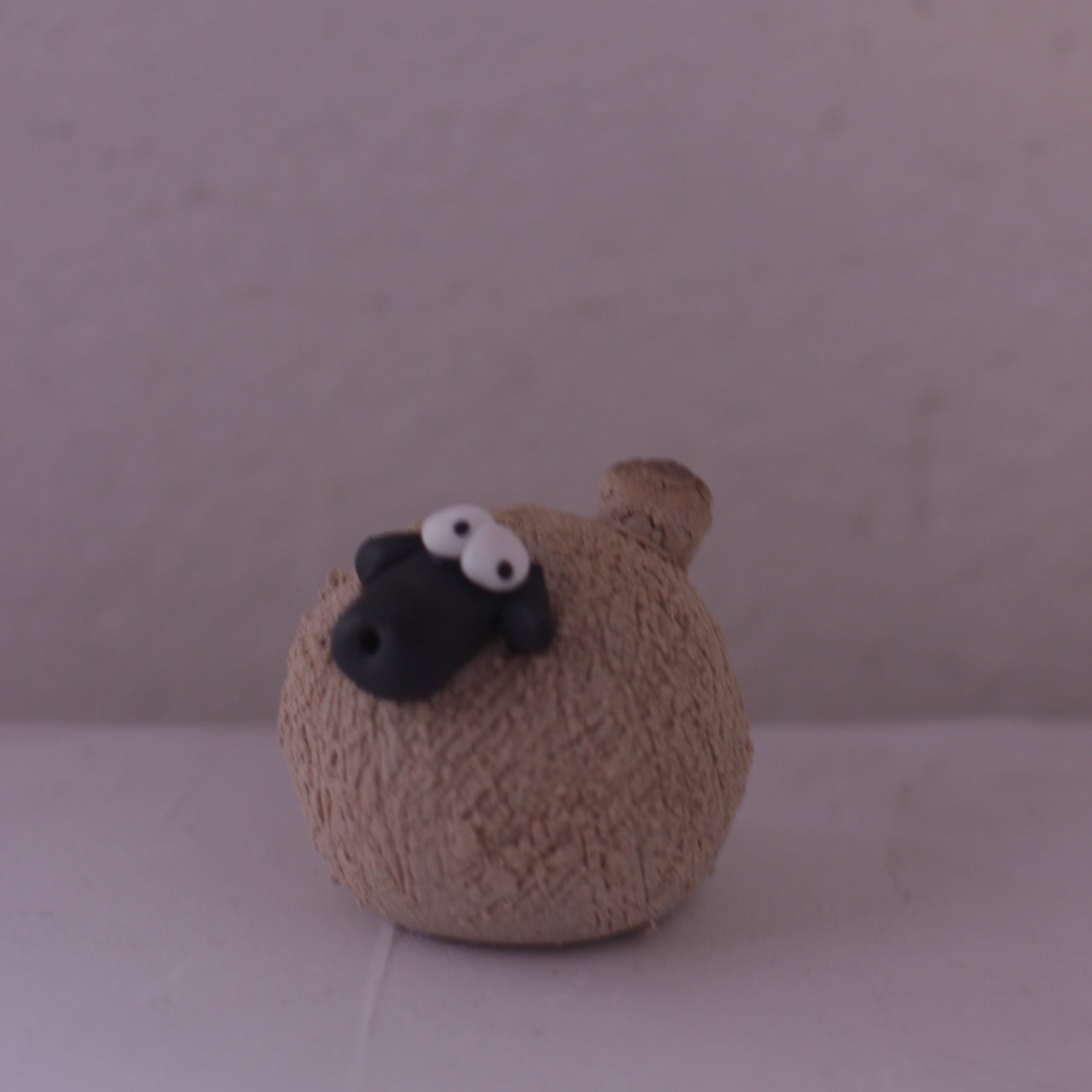 Handmade pottery animal figurine of a round sheep with textured beige body and black face